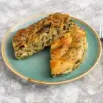 Golden filo dough dessert roll on a green plate. Sliced and ready to serve.
