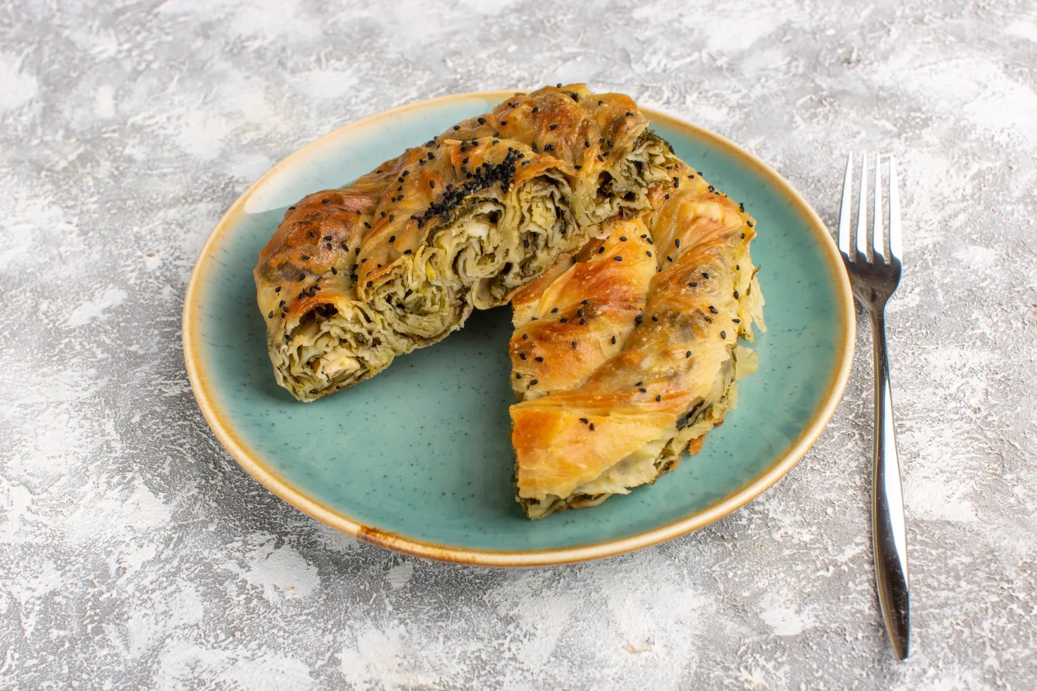 Golden filo dough dessert roll on a green plate. Sliced and ready to serve.