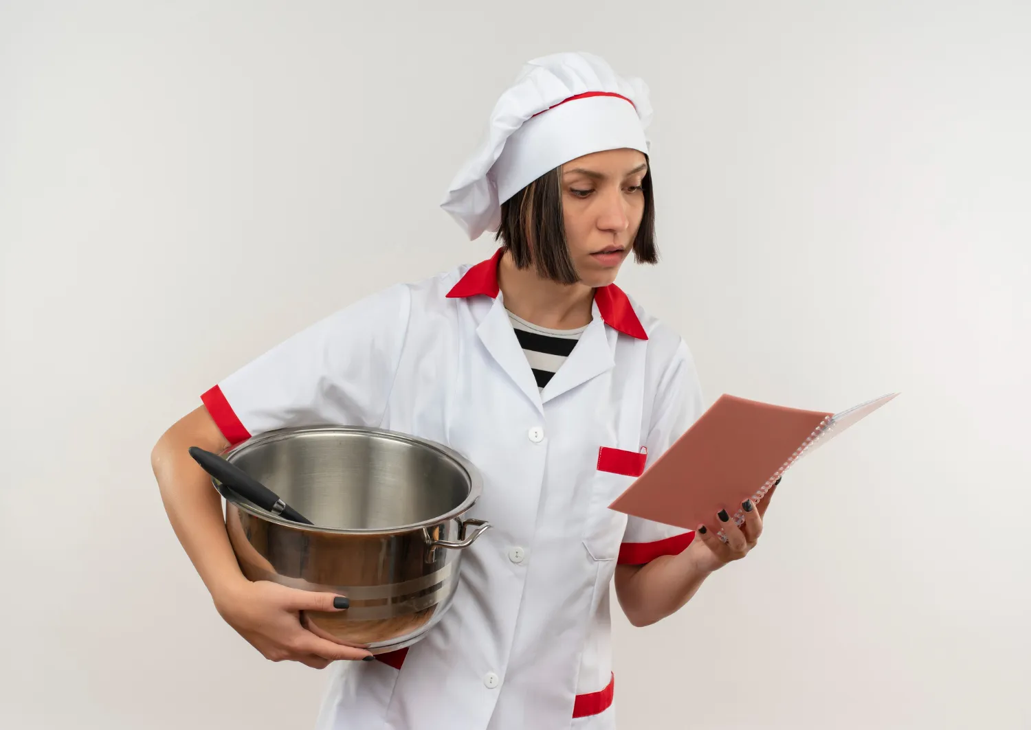 Female chef in uniform reading a recipe notebook while holding a mixing bowl — illustrating how to judge a recipe before cooking.