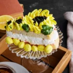 A slice of lemon lush dessert on a glass plate. Topped with whipped cream and yellow frosting.