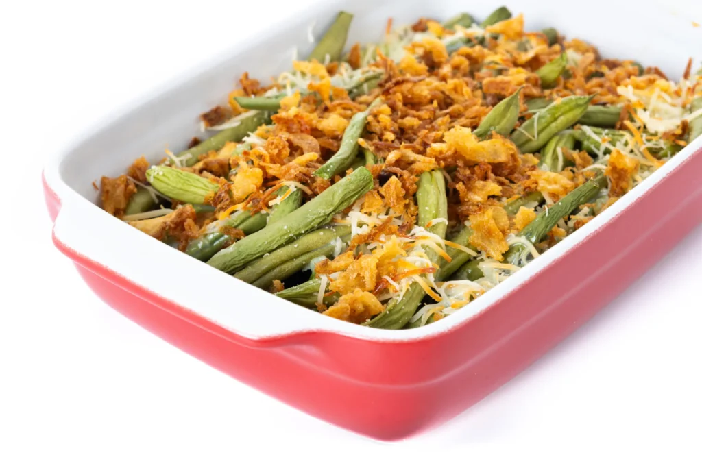 Freshly baked Campbell’s Green Bean Casserole in a white dish, topped with golden crispy onions and surrounded by key ingredients.