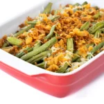 Freshly baked Campbell’s Green Bean Casserole in a white dish, topped with golden crispy onions and surrounded by key ingredients.