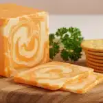Block and slices of Colby Jack Cheese on wooden board with crackers