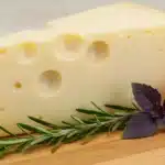 Wedge of Asiago cheese on a board with herbs and tomato