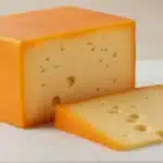 Block of Muenster cheese with orange rind on cutting board