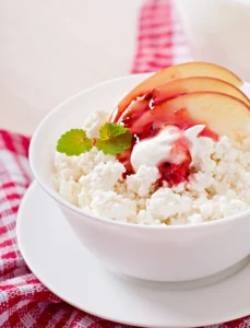 A variety of cottage cheese desserts, including cheesecake, pudding, and a fruit bowl, arranged on a table.