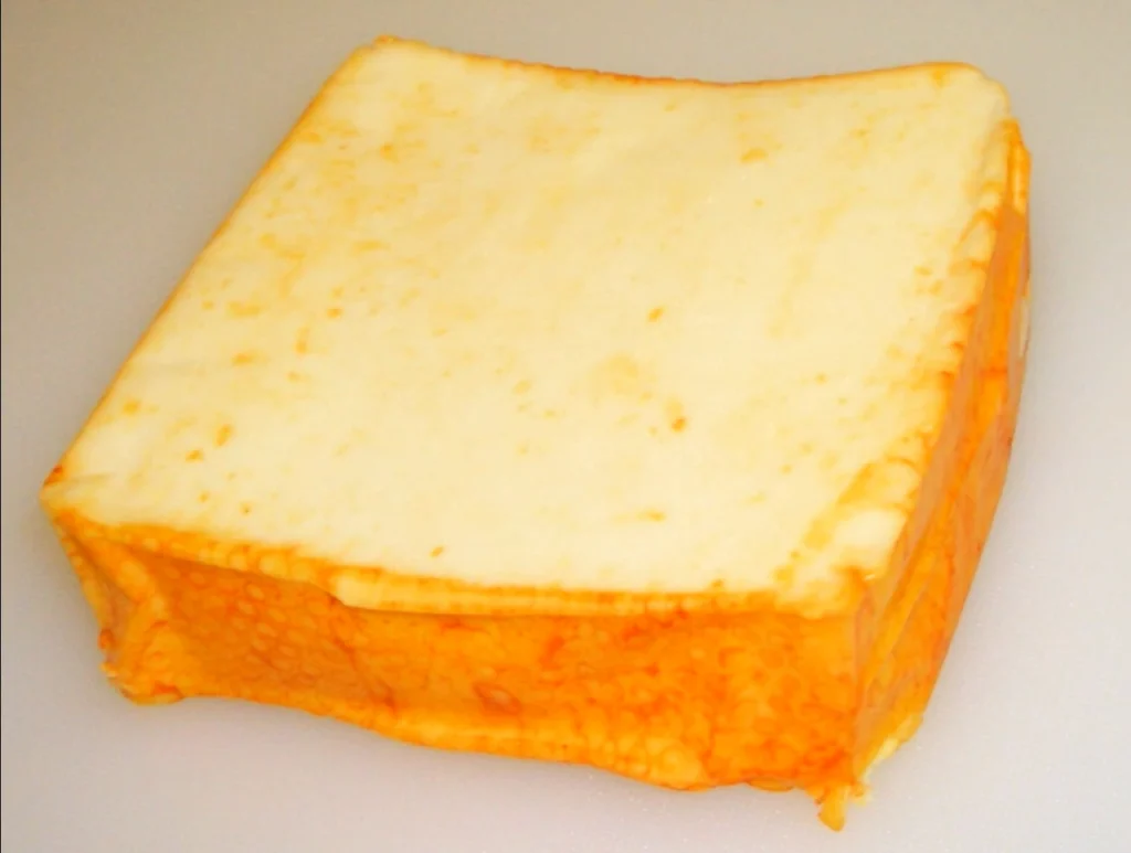 Close-up of sliced Muenster cheese with a smooth white interior and an orange rind, arranged on a wooden board.