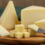 White cheddar cheese block and shredded pieces on a wooden board, showcasing its creamy texture and rich flavor.
