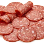 Sliced beef pepperoni stacked in a pile, showcasing its rich red color and marbled texture with flecks of fat.