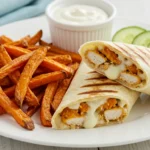 Grilled cheesy garlic chicken wrap served with sweet potato fries and cucumber slices on a wooden plate.