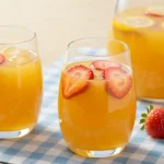 Glasses of strawberry mango lemonade with strawberries and ice on a picnic cloth