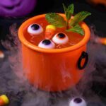 Bright orange Halloween punch in mini cauldron with floating gummy eyeballs