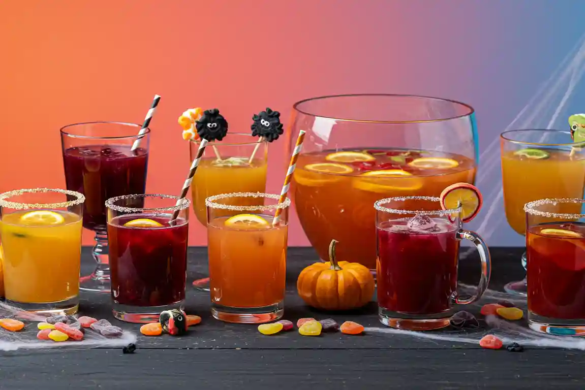 Five Halloween punches on black table with themed garnishes and lighting