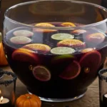 Halloween punch recipe in a glass bowl with citrus and sugar-rimmed glasses